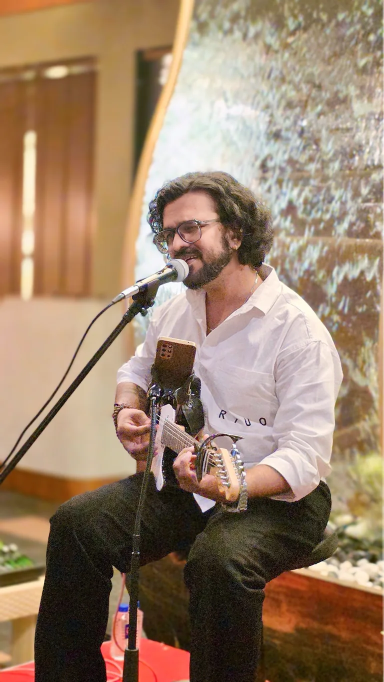 Aniket Patel performing live, seated with a guitar at a microphone
